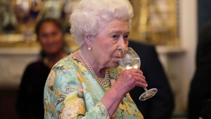 regina elisabeta intr-o rochie inflorata in timp ce bea vin dintr-un pahar transparent