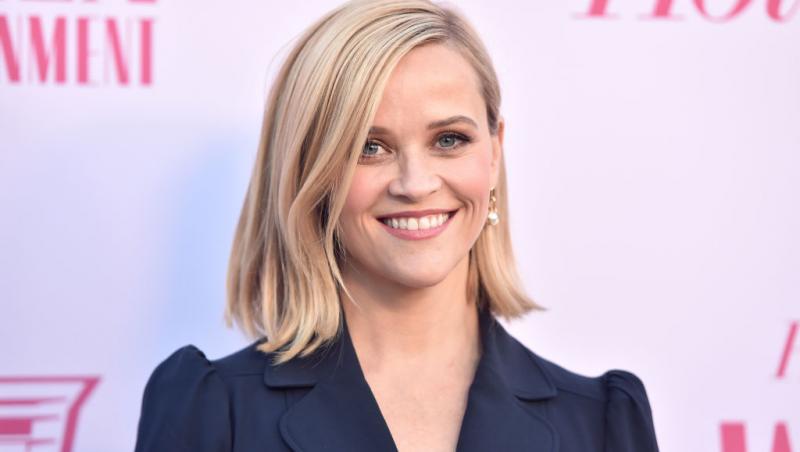 Reese Witherspoon imbracata intr-o tinuta inchisa la culoare, zambitoare