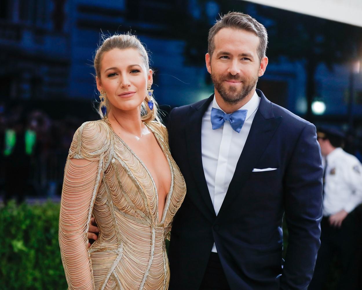 blake lively si ryan reynolds pe covorul rosu, ea intr-o rochie aurie, el intr-un costum bleumarin cu papion albastru