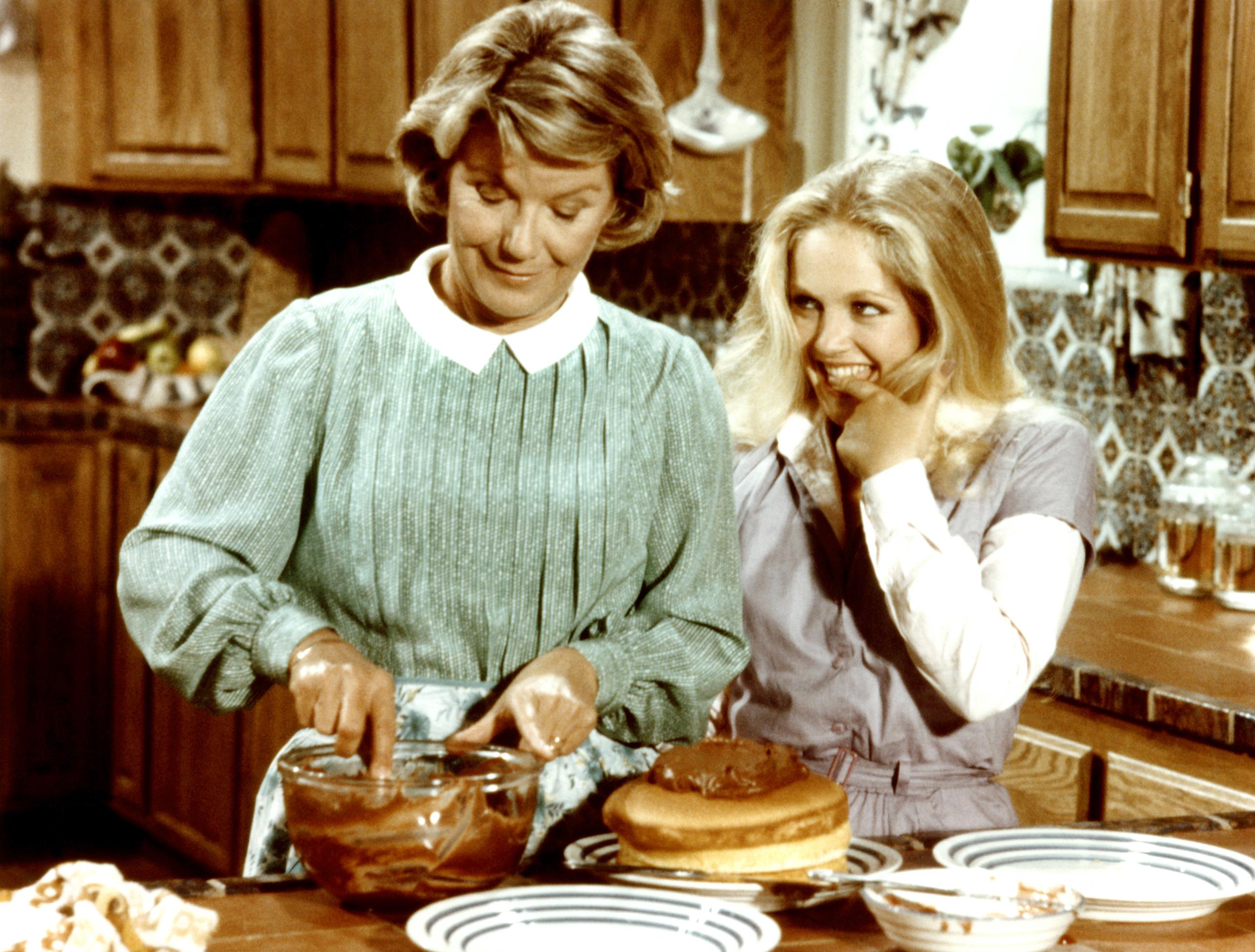 lucy ewing, în serialul dallas, în bucătărie cu bunica ei. îmbrăcată într-o bluză albă, cu vestă gri, părul blond lung