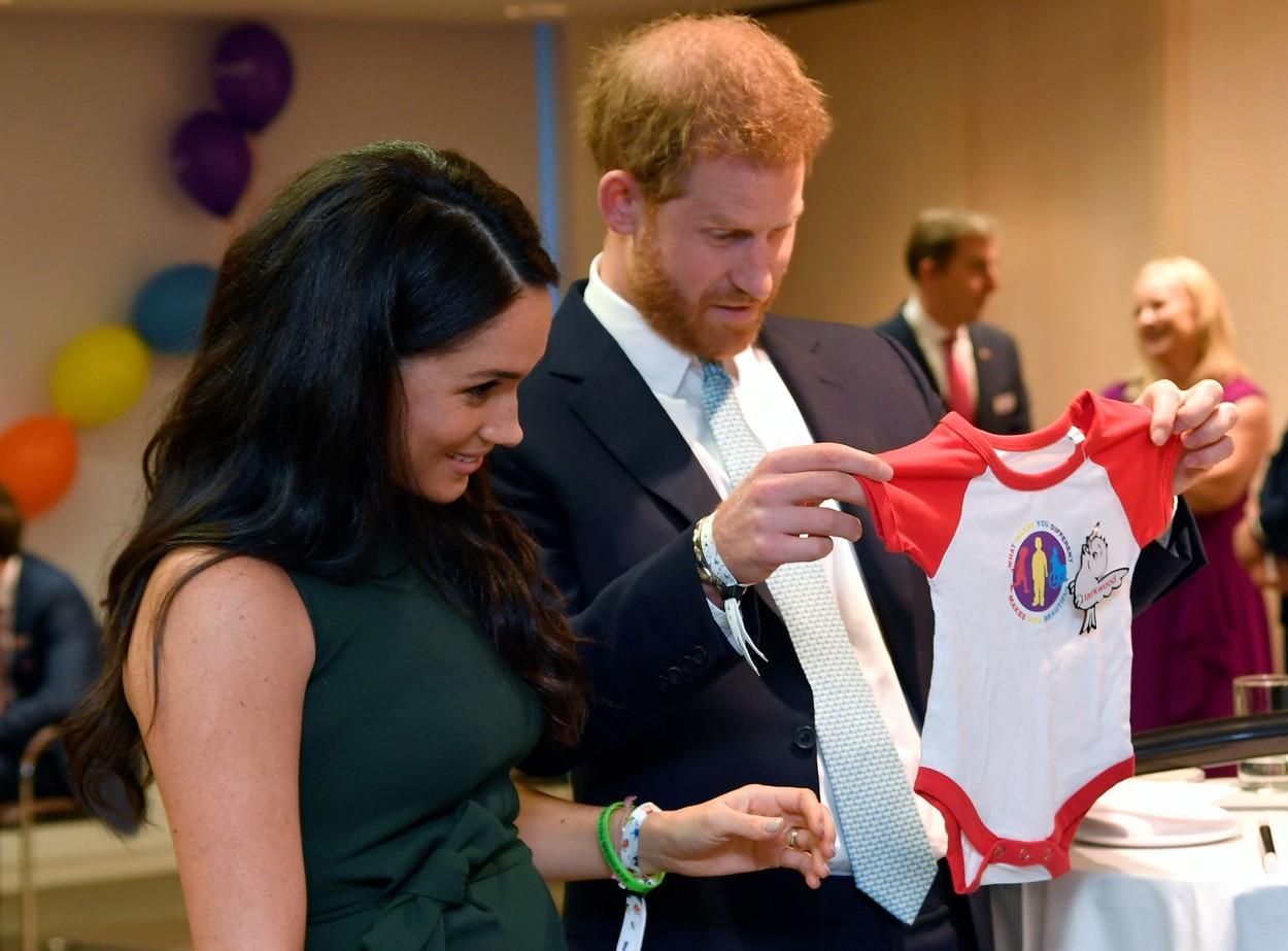 meghan markle si printul harry tinand in mana un body de bebelus