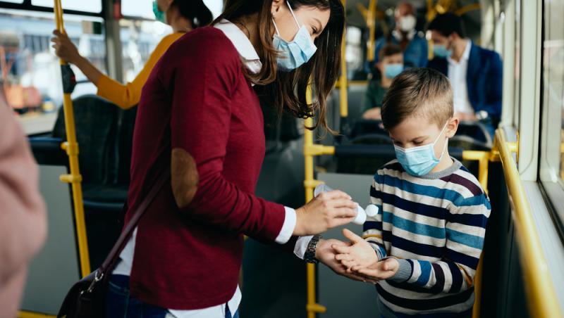 femeie si copil in autobuz cu mastile puse si se dau cu dezinfectant