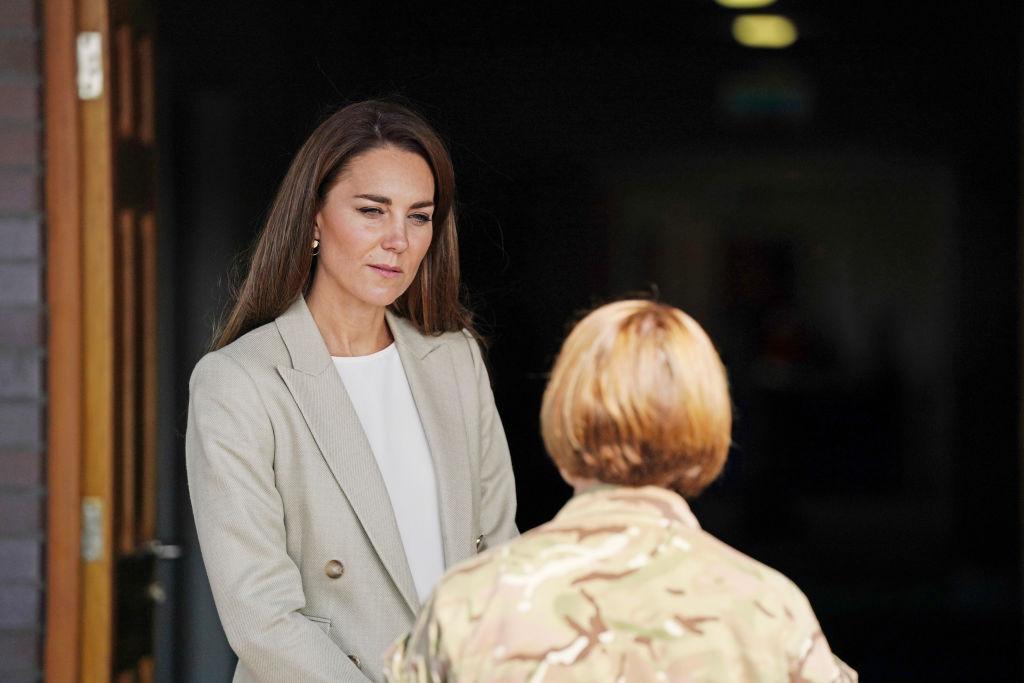 Kate Middleton, intr-un sacou deschis la culoare, si o alta persoana in plan
