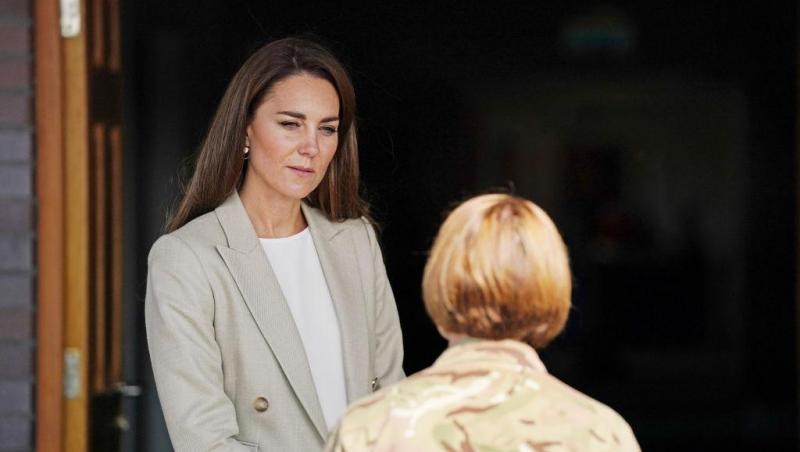 Kate Middleton, intr-un sacou deschis la culoare, si o alta persoana in plan