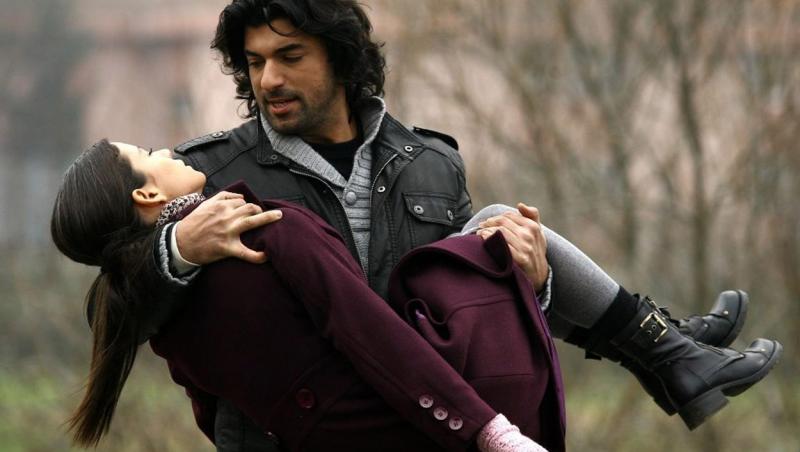 actorul turc imbracat elegant, in palton, tinand o femeie pe brate