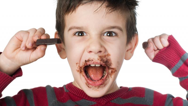 copil care e vesel si zambeste cu dintii dupa ce a mancat ciocolata