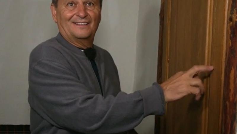 Nea Marin, cu o bluză gri, lângă ușă