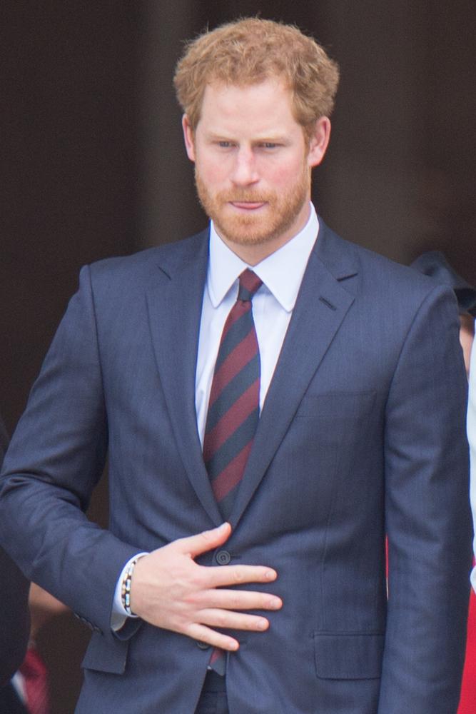 Prințul Harry, îmbrăcat cu un costum închis la culoare, o cămașă albă și o cravată cu dungi negre și roșii în diagonală