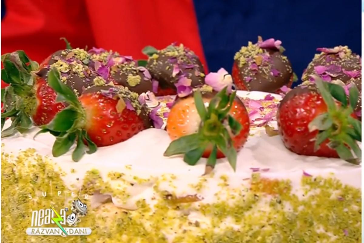 Pentru un aspect spectaculos, tortul se decorează cu căpșuni trase în ciocolată și pudrate cu fistic și petale de trandafiri