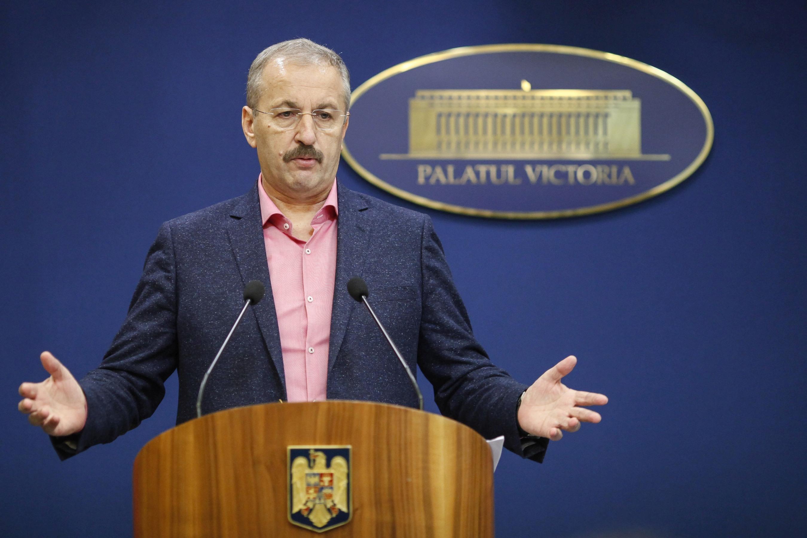 Vasile Dîncu în cămașă roz și sacou albastru, gesticulează și vorbește la microfon