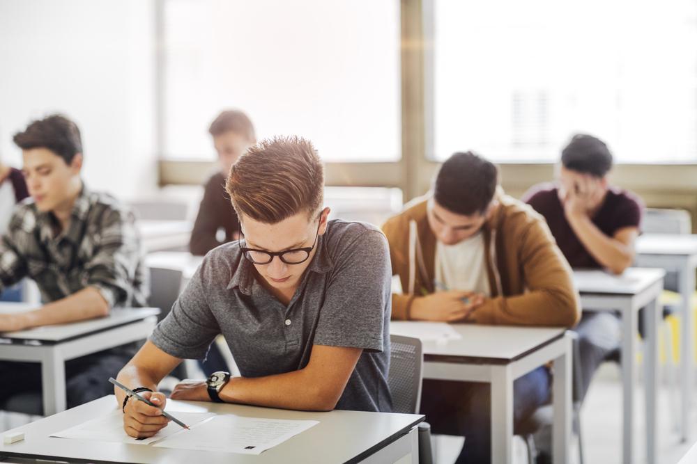 tineri asezati in banci in timpul unui examen