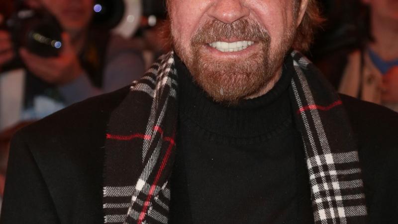 Chuck Norris în haine negre și zâmbește