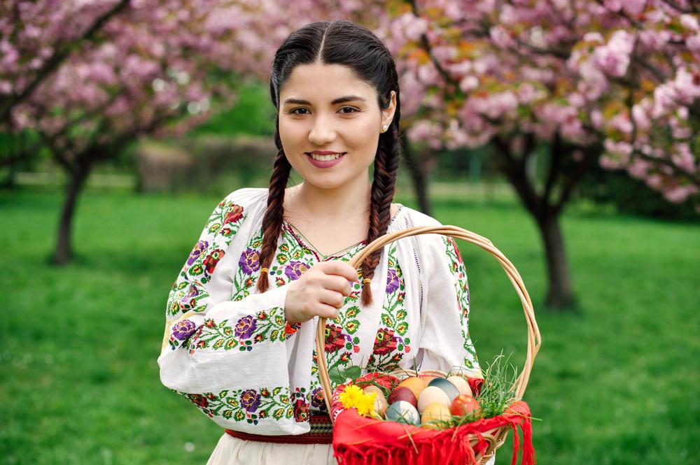 tanara imbracata in costum traditional romanesc cu un cos cu oua de paste