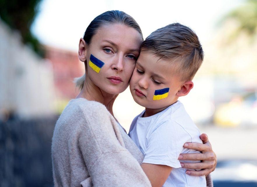 mama care isi tine in brate copilul, ambii cu steagul ucrainei desenat pe obraz