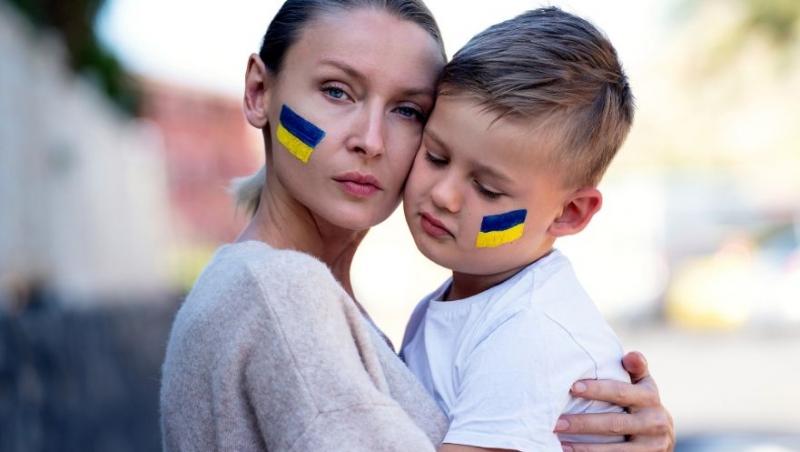 mama care isi tine in brate copilul, ambii cu steagul ucrainei desenat pe obraz