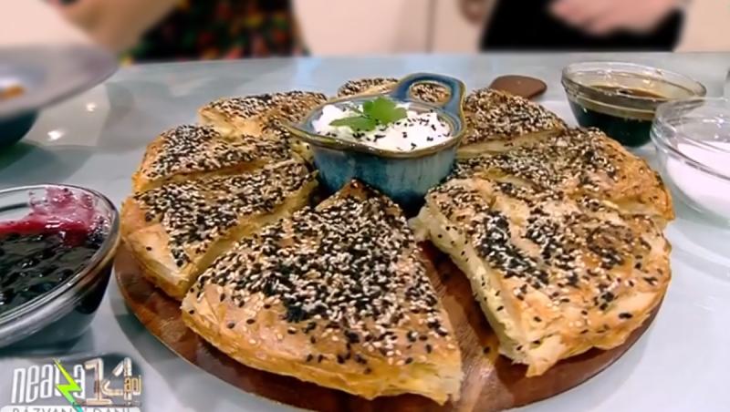 Plăcintă turcească Borek feliată pe un platou, alături de un bol cu iaurt