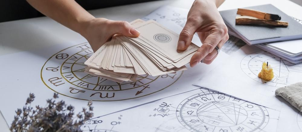 femeie cu carti de tarot in mana si cu un desen cu cele 12 zodii ale horoscopului