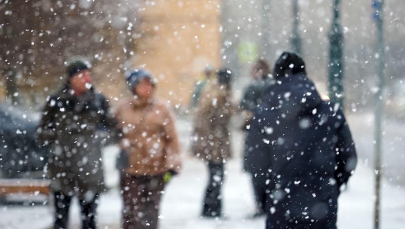 fotogrfie cu o stradă ăe care s-a asternut ninsoarea si oameni care trec prin zapada