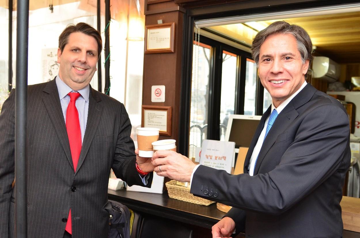 imagine cu doi directori in sacou gri si cravata rosie care beau cafea la un interviu de angajare
