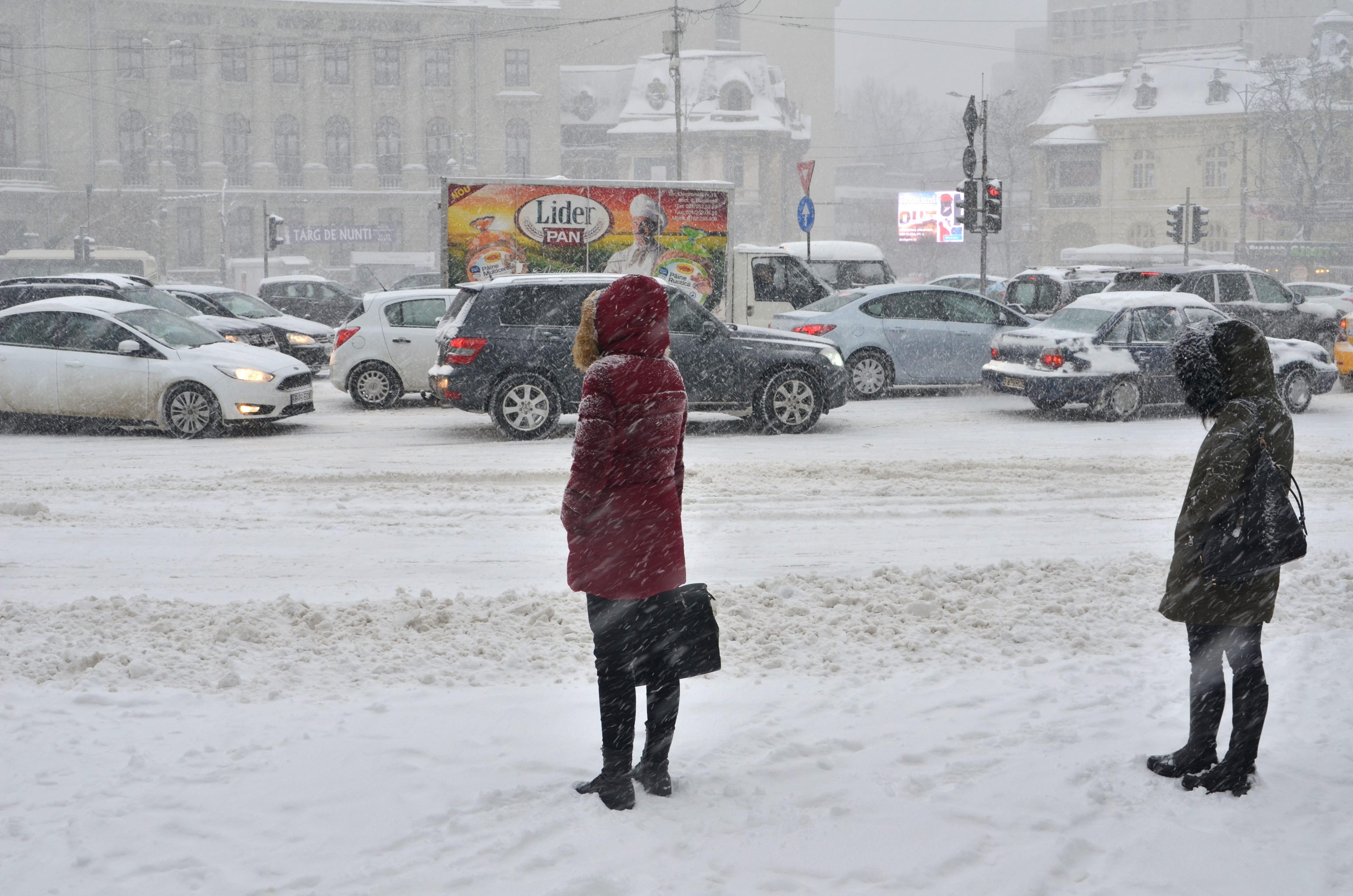 fotogrfie cu o stradă pe care s-a asternut ninsoarea si oameni care trec prin zapada