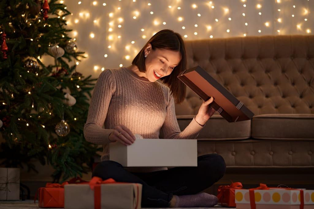 O fată care deschide un cadou lângă bradul de Crăciun