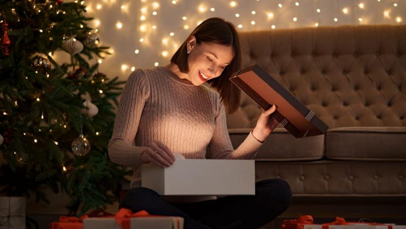 O fată care deschide un cadou lângă bradul de Crăciun