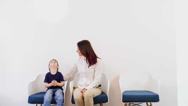 Imagine cu o mamă și un copil care nu mai are răbdare să aștepte pe scaun.