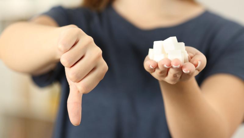 Imagine cu o femeia care exprimă refuzul de a consuma zahăr printr-un semn de negare al mâinii