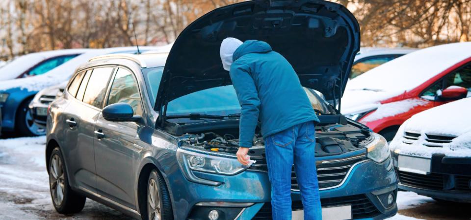 Imagine cu un bărbat care verifică mașina pe timp de iarnă. Acesta a ridicat capota.