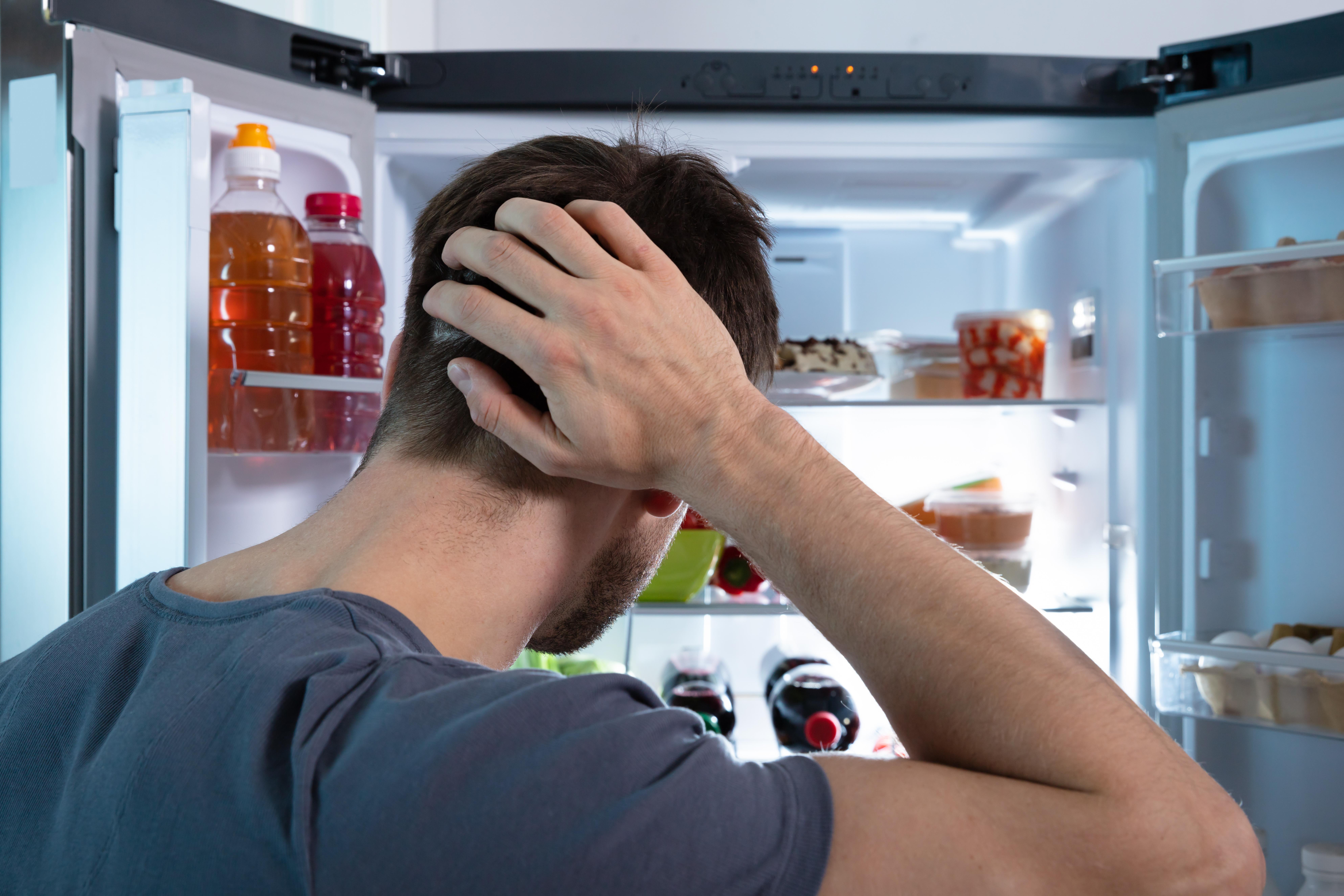 Imagine cu un bărbat care nu știe ce să mai facă să combată mirosul neplăcut din frigider. Acesta își ține o mână în cap.