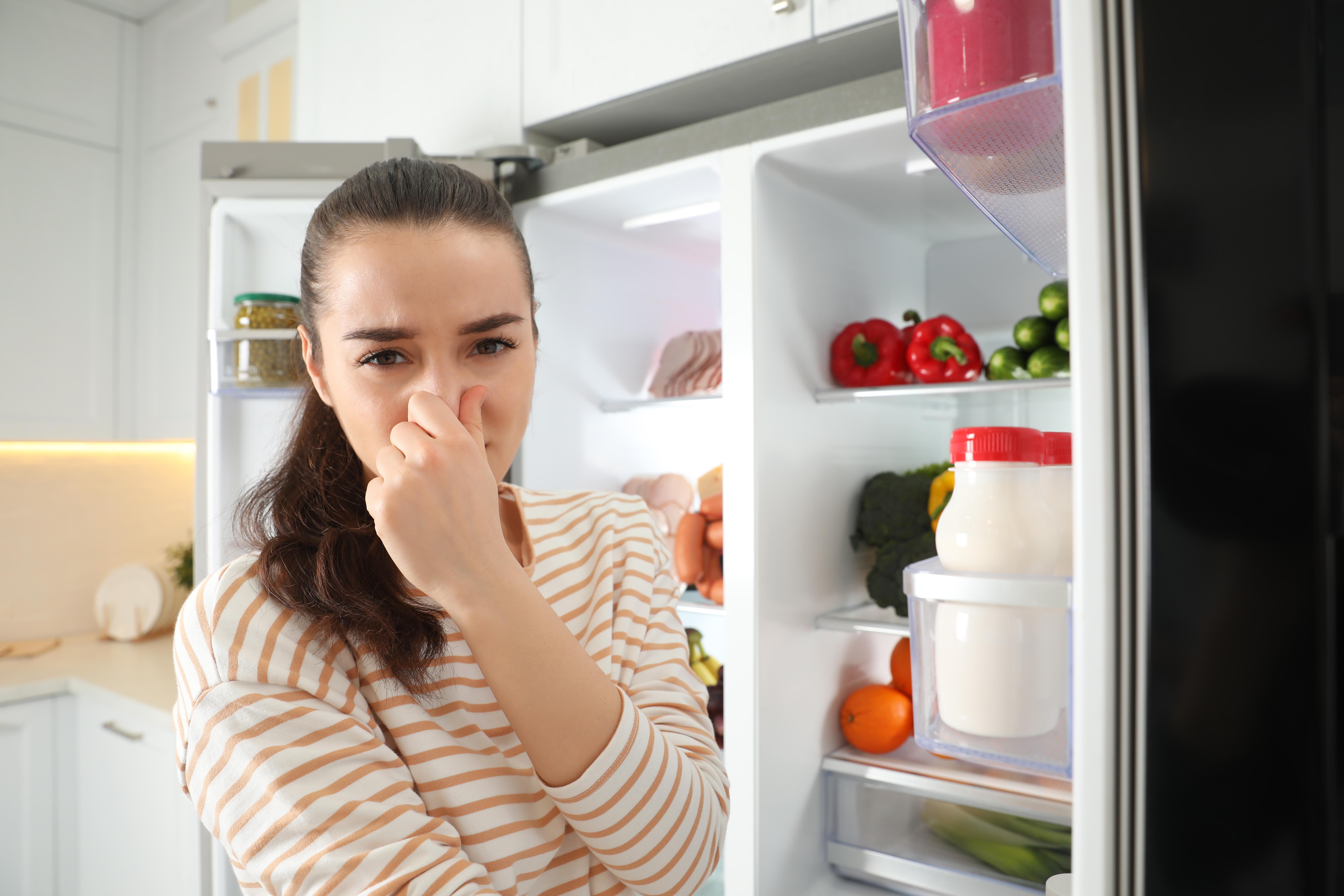 Imagine cu o femeie care se ține de nas din cauza mirosului neplăcut din frigider.