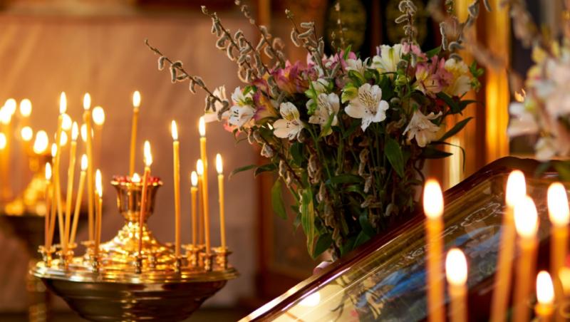 Imagine cu lumânări, flori și o icoană în Biserică.