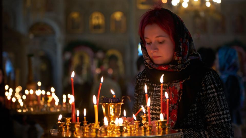 Imagine cu o femeie credincioasă care aprinde o lumânare în Biserică.