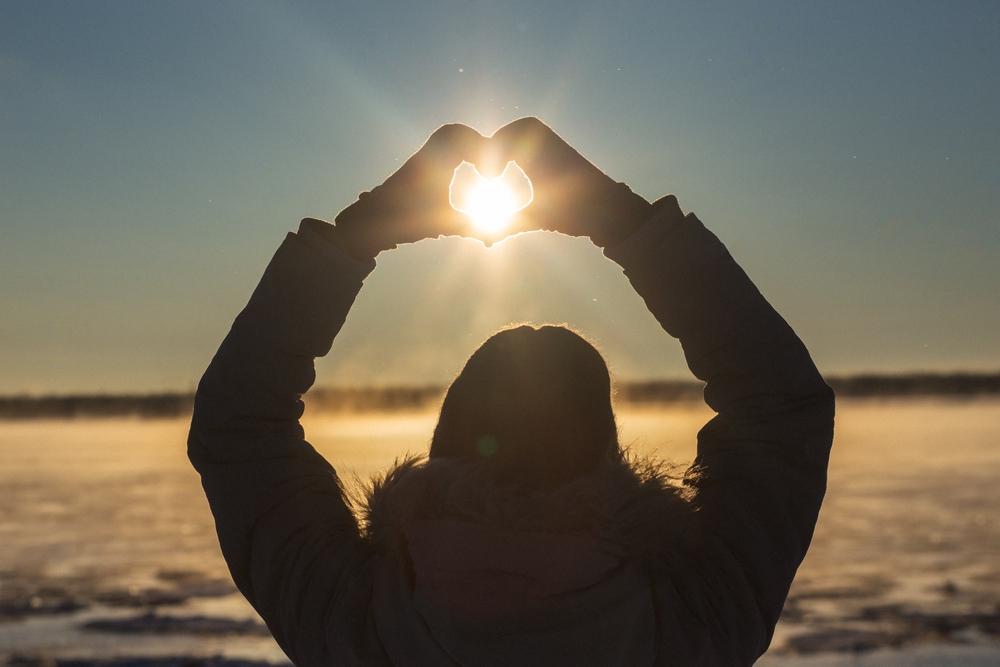 femeie care formează o inimă cu mâinile și curpinde soarele în mijloc, în timpul solstițiului de iarnă