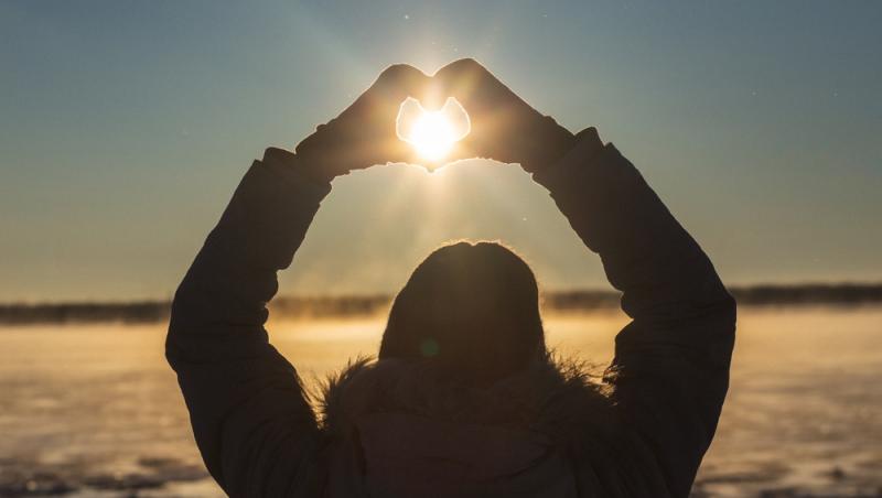 femeie care formează o inimă cu mâinile și curpinde soarele în mijloc, în timpul solstițiului de iarnă