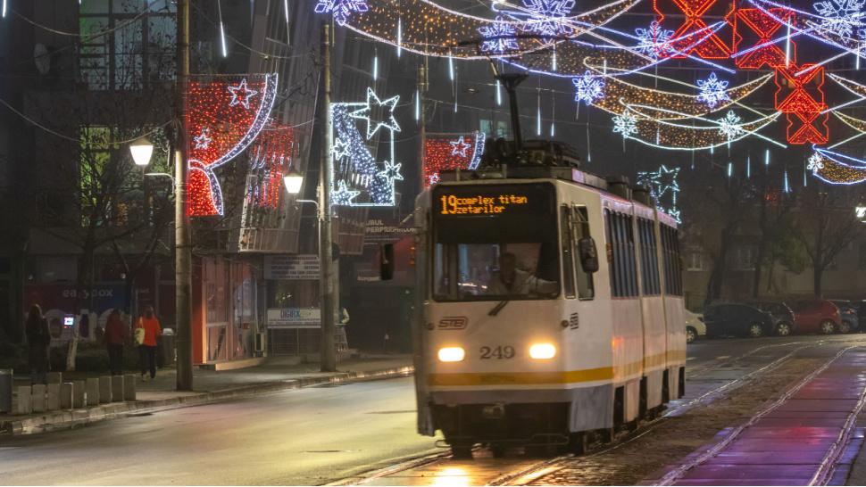 Imagine cu un tramvai care circulă pe timp de seară. Orașul este împodobit pentru Sărbători