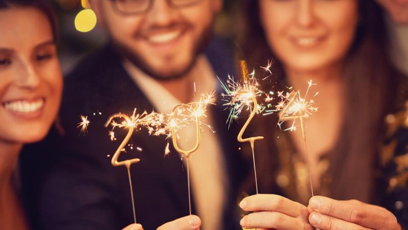 femei și bărbați îmbrăcați de petrecere ținând în mână artificii care formează 2024