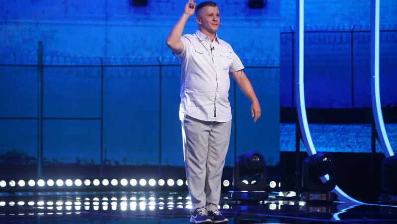 Dan Boldiszar în cămașă și pantaloni cu mâna ridicată pe scenă