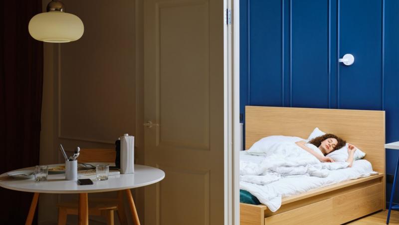 femeie într-un pat matrimonial cu lenjerie albă și o cameră cu pereți albastru cerneală