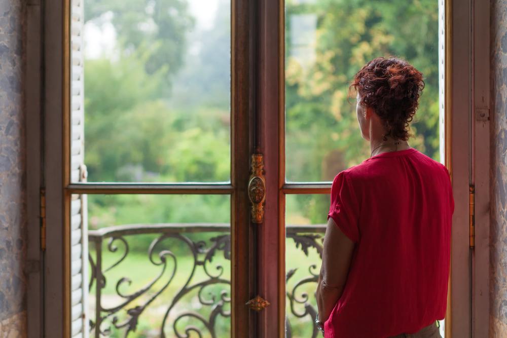 femeie in tricou rosu care se uita pe fereastra
