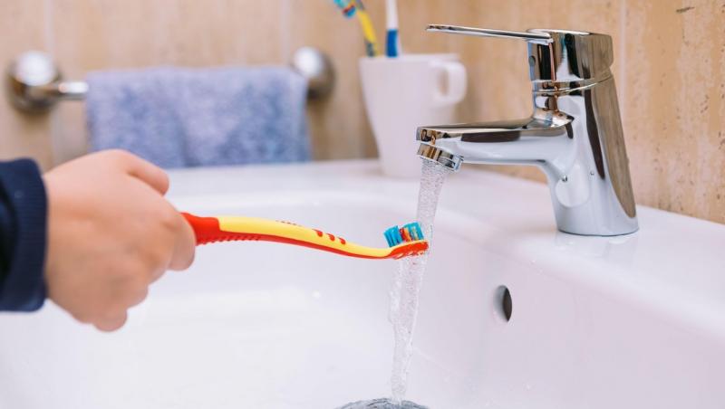imagine cu mana unei persoane care uda o periuta de dinti in chiuveta