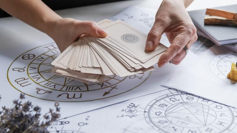 o femeie cu carti in mana si instrumente specifice astrologiei intinse pe o masa