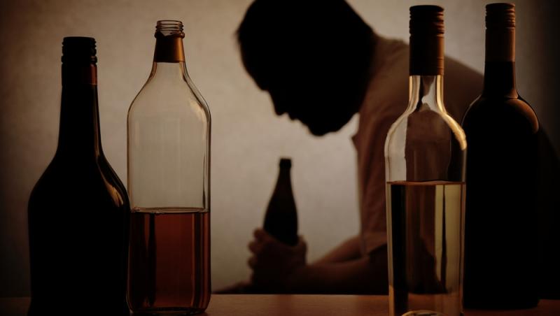 umbra unui bărbat și sticle de alcool în prim-plan