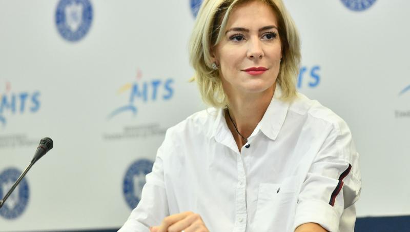 Roxana Ciuhulescu într-o conferință de presă, în fața unui microfon, îmbrăcată într-o cămașă albă