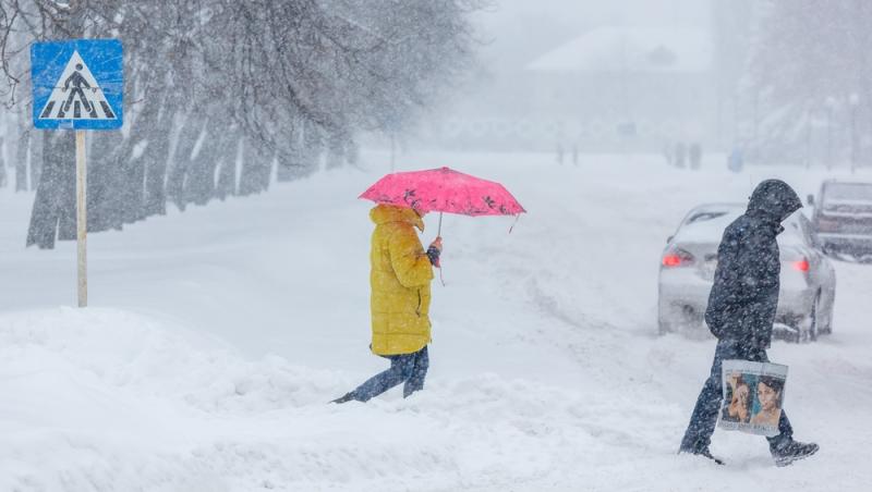 Două persoane mergând prin zăpadă pe stradă