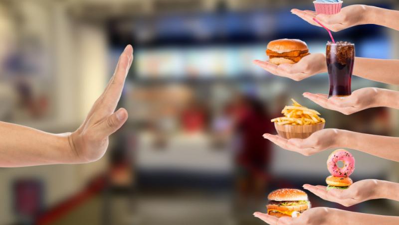 Imagine cu mâna unei persoane care refuză mâncarea de tip fastfood.