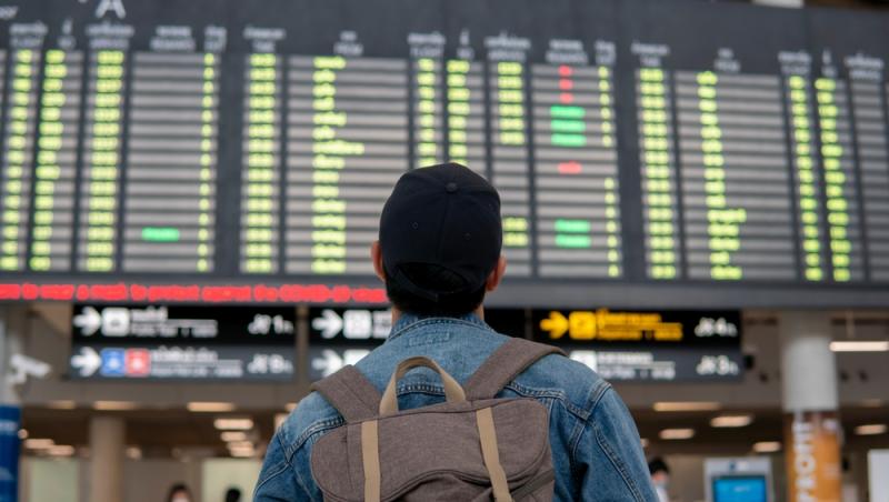 bărbat cu rucsac în spate care privește ecranul cu plecările în aeroport