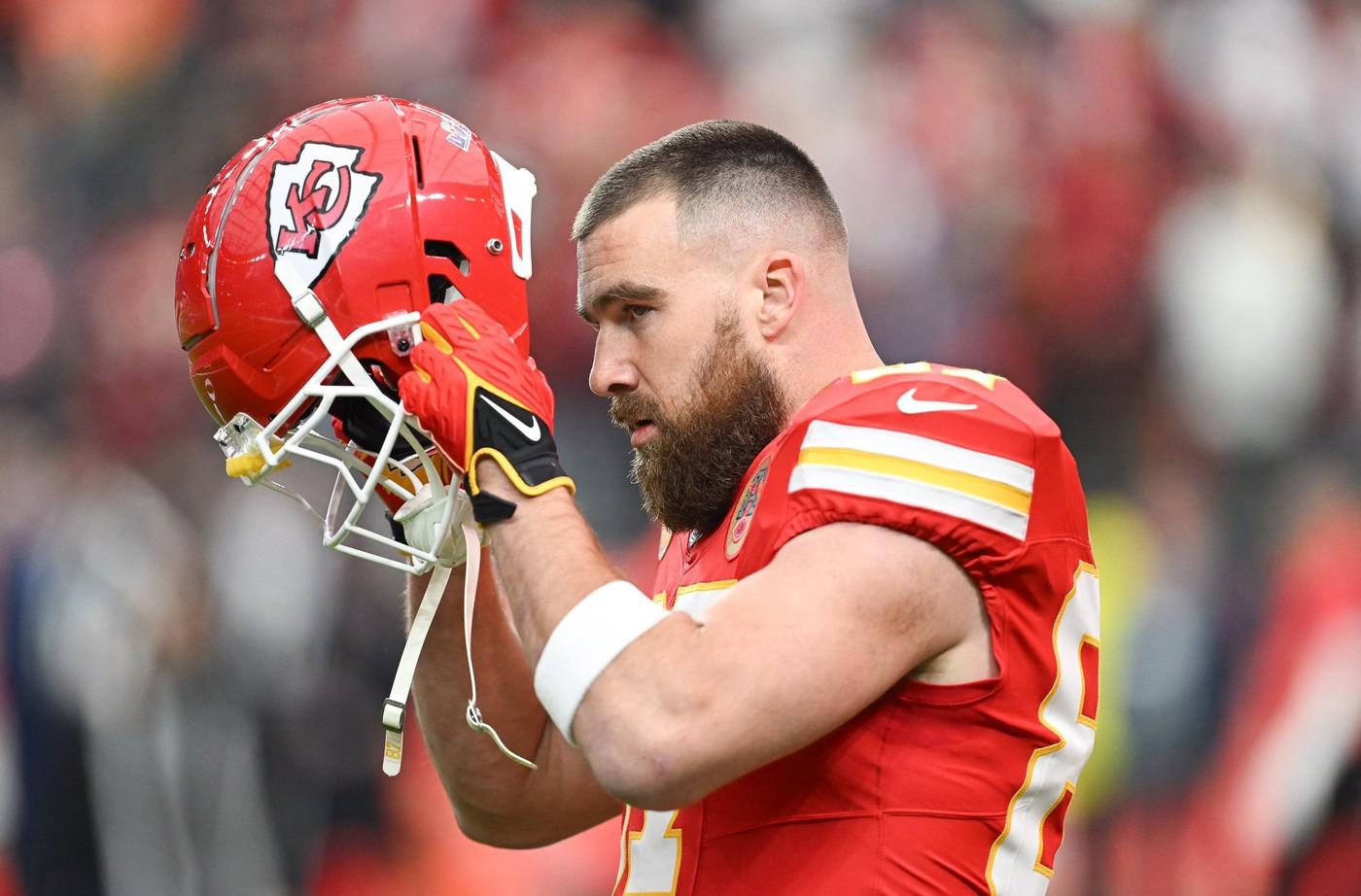 travis kelce in echipamentul sportiv kansas city chiefs, in timpul unui meci de fotbal american, cu casca in mana