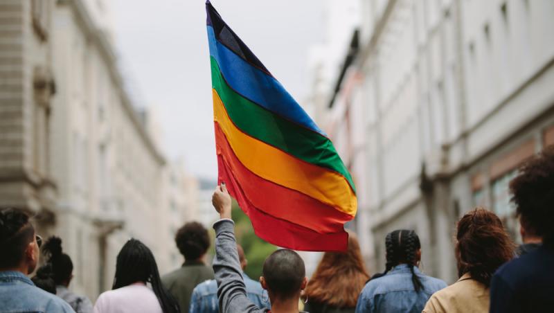 omanei pe stradă care stau cu spatele și poartă un steac în culorile curcubeului (LGBTQ)