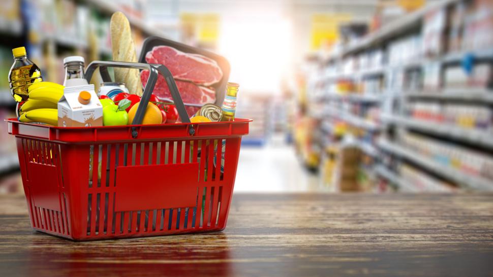 Imagine cu un coș de cumpărături în care se regăsesc mai multe alimente precum: lapte, fructe, ulei, legume, etc.